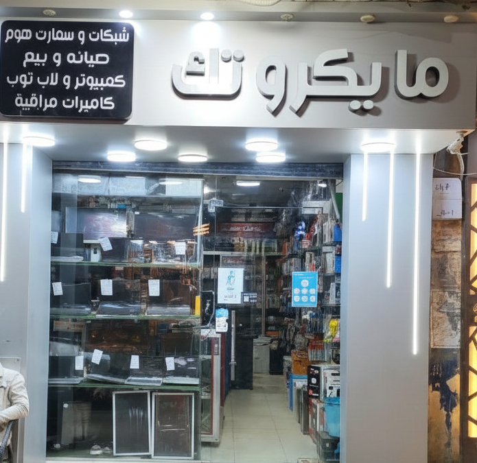 Storefront with Arabic signage and people outside, likely in a shopping area.